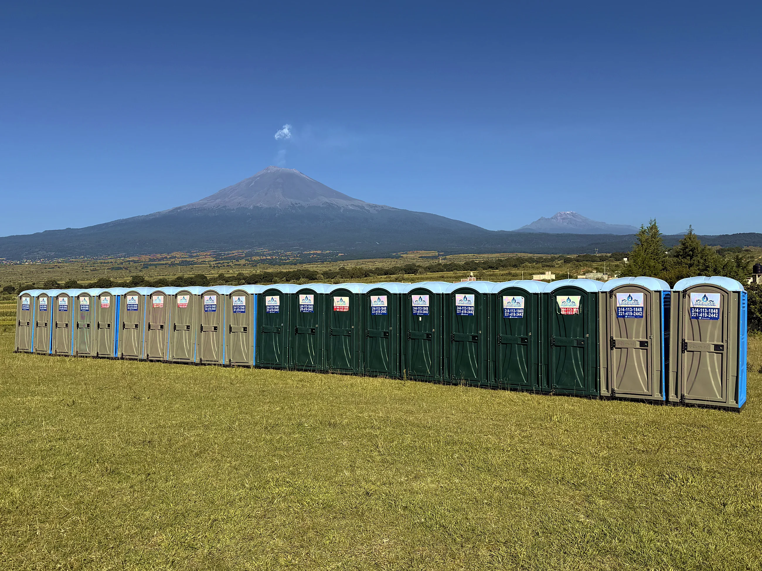 Fila de sanitarios portátiles Sani Móvil en un campo, con el volcán Popocatépetl al fondo